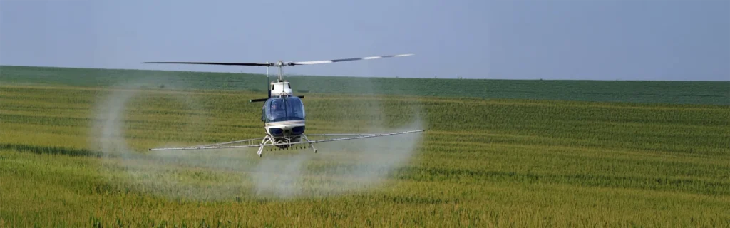 Helicopter spraying crops over a green agricultural field.